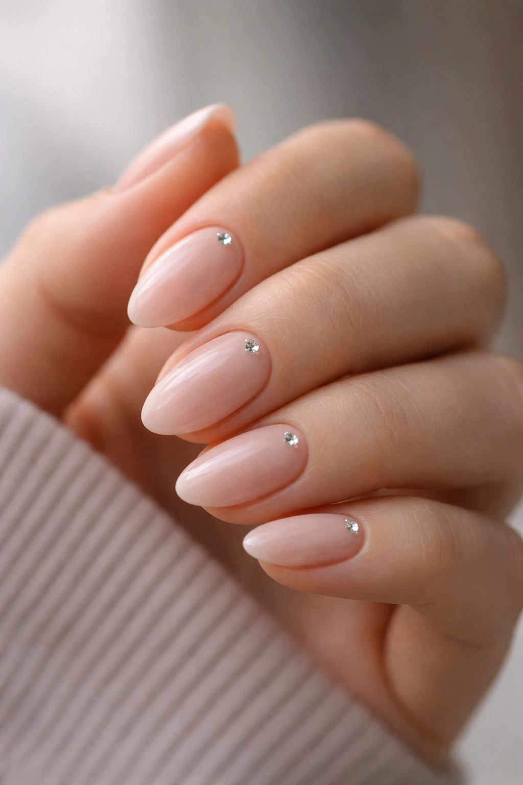 Close-up of short almond nails with a single rhinestone near the cuticle