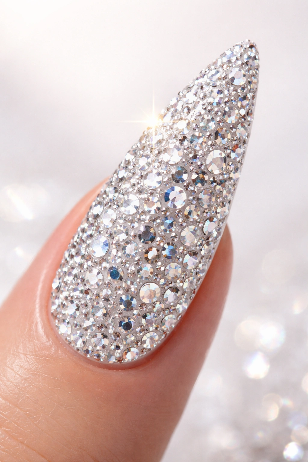 Close-up of a stiletto nail fully covered in rhinestones on white base