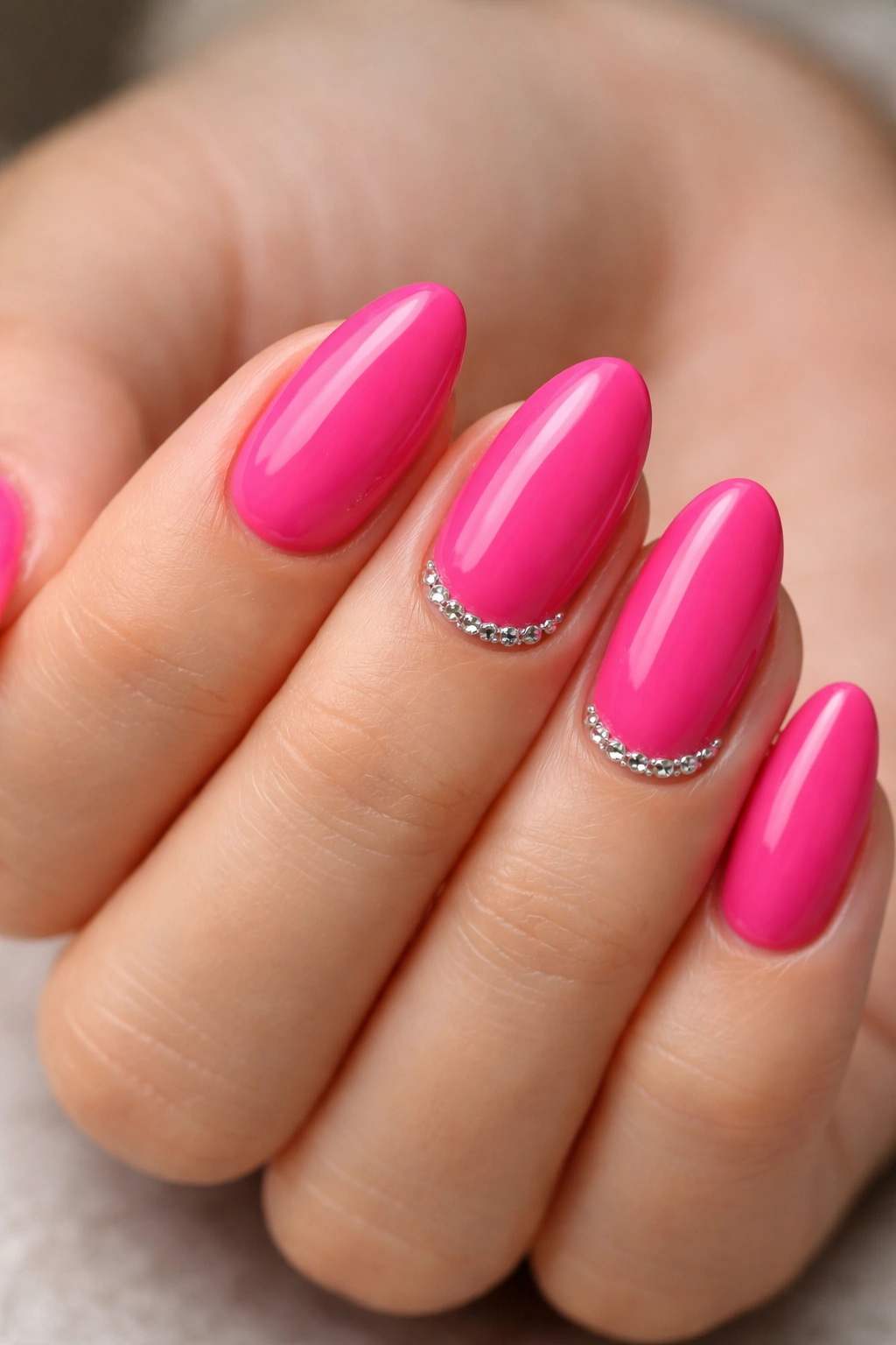 Hot pink almond nails with rhinestones at the cuticle on accent nails
