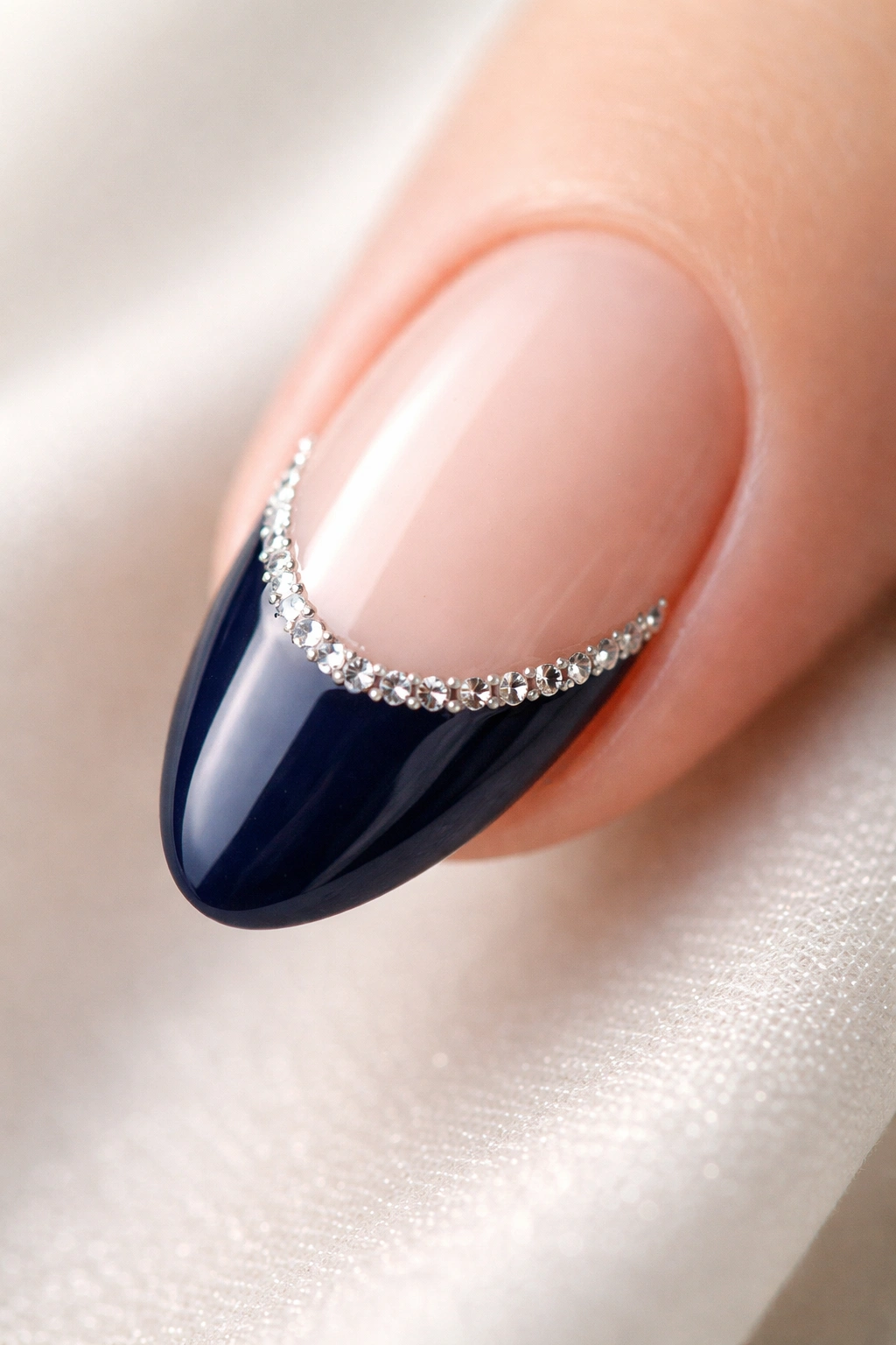 Close-up of a short almond nail with navy tip and a delicate row of rhinestones along the smile line
