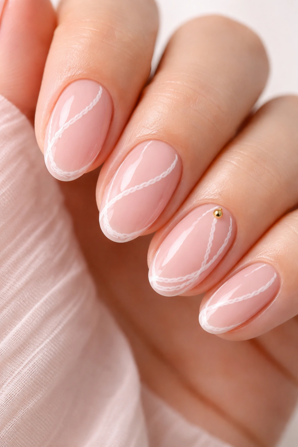 Short almond nails with sheer pink base and white rope curves with a tiny gold bead