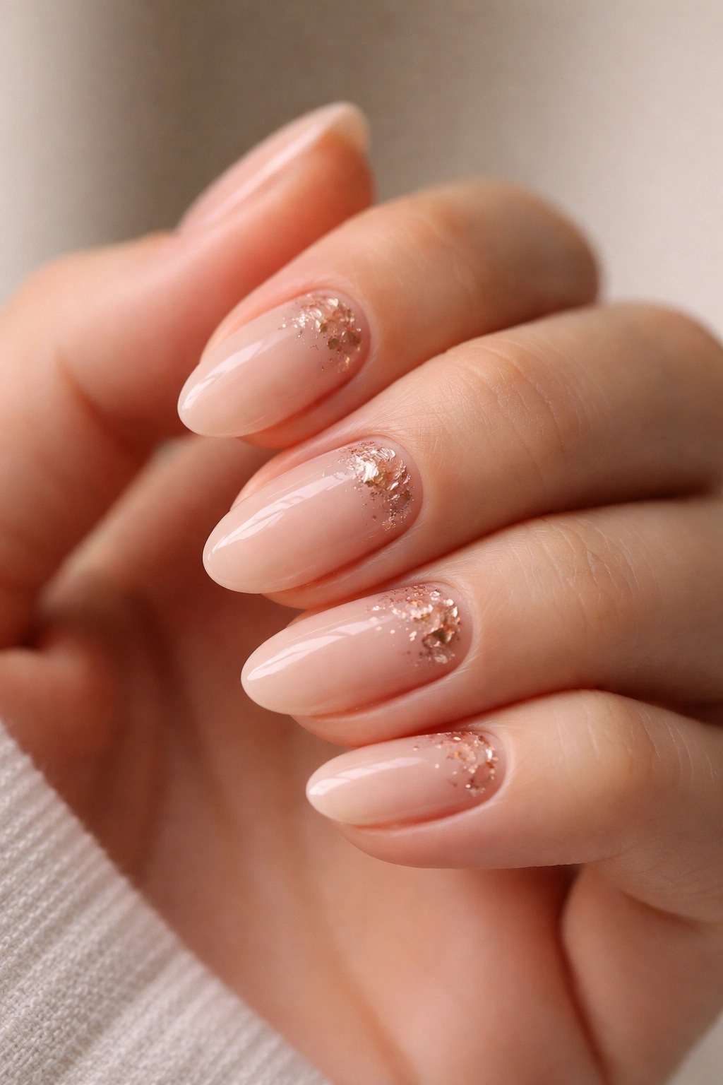 Close-up of rose gold foil accents on nude short almond nails with negative space