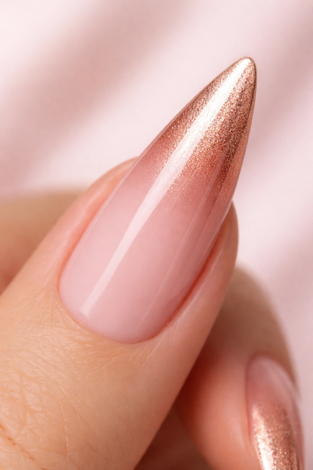 Close-up of a stiletto nail with a soft pink to rose gold gradient on a neutral background