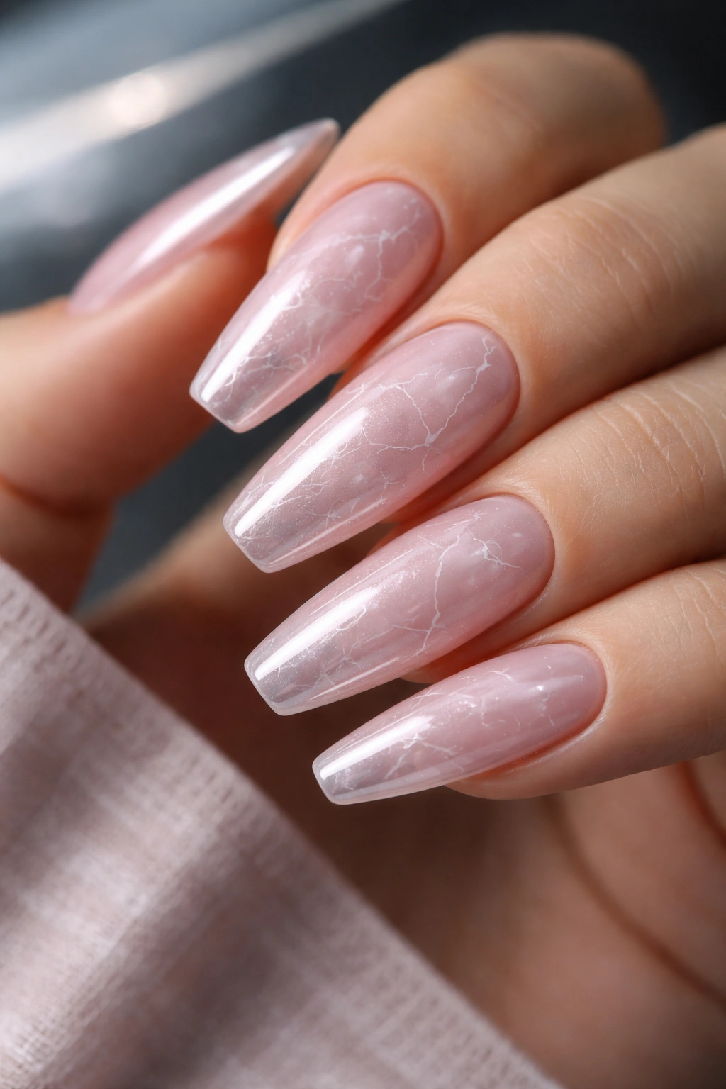 Close-up of rose quartz chrome nails with fine white veins on ballerina nails