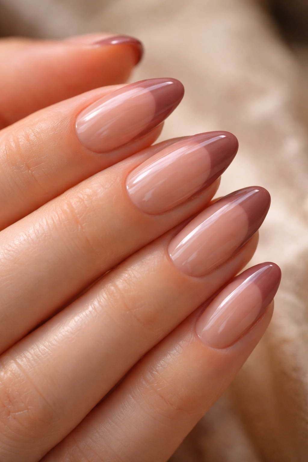 Almond nails with rosy brown French tips over jelly nude base with high-gloss finish.