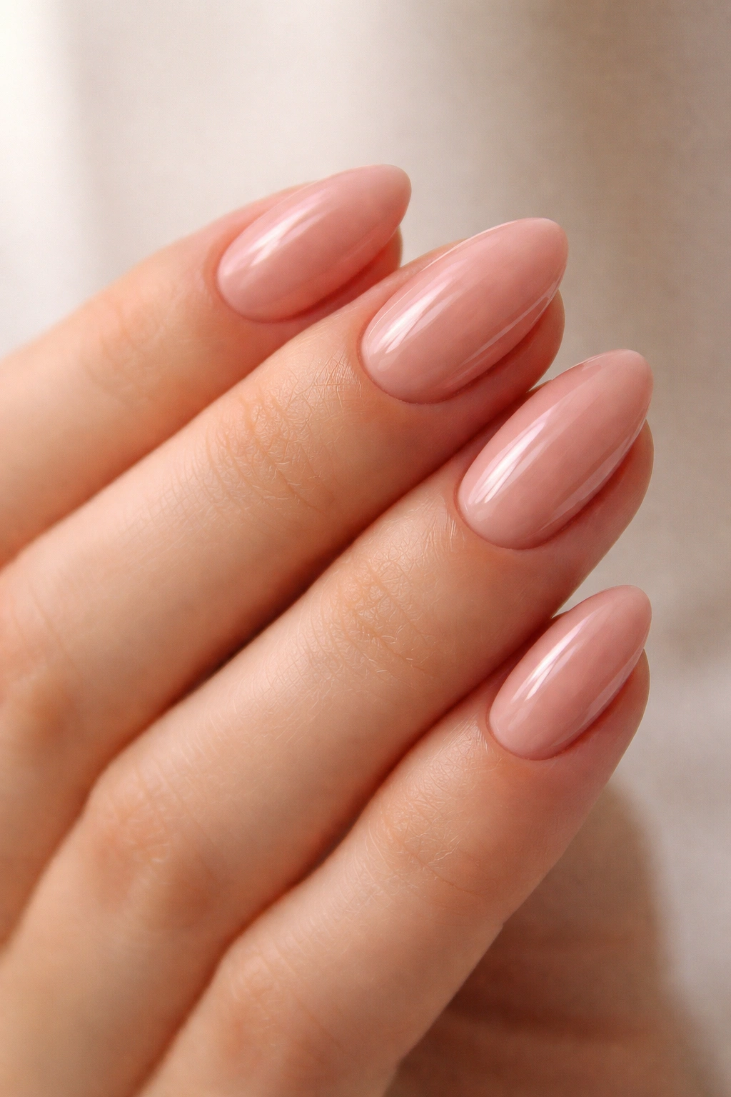 Close-up of rosy nude short almond nails with glassy high-gloss finish