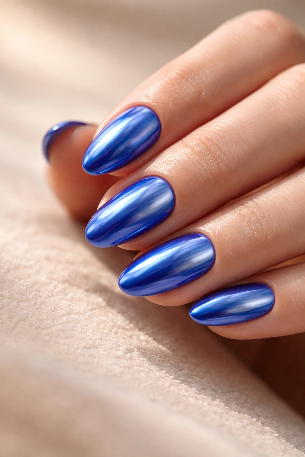 Close-up of short almond nails with royal blue base and chrome glaze