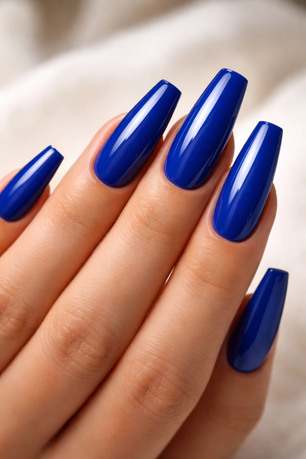 Close-up of royal blue coffin nails with a glossy finish on a manicured hand