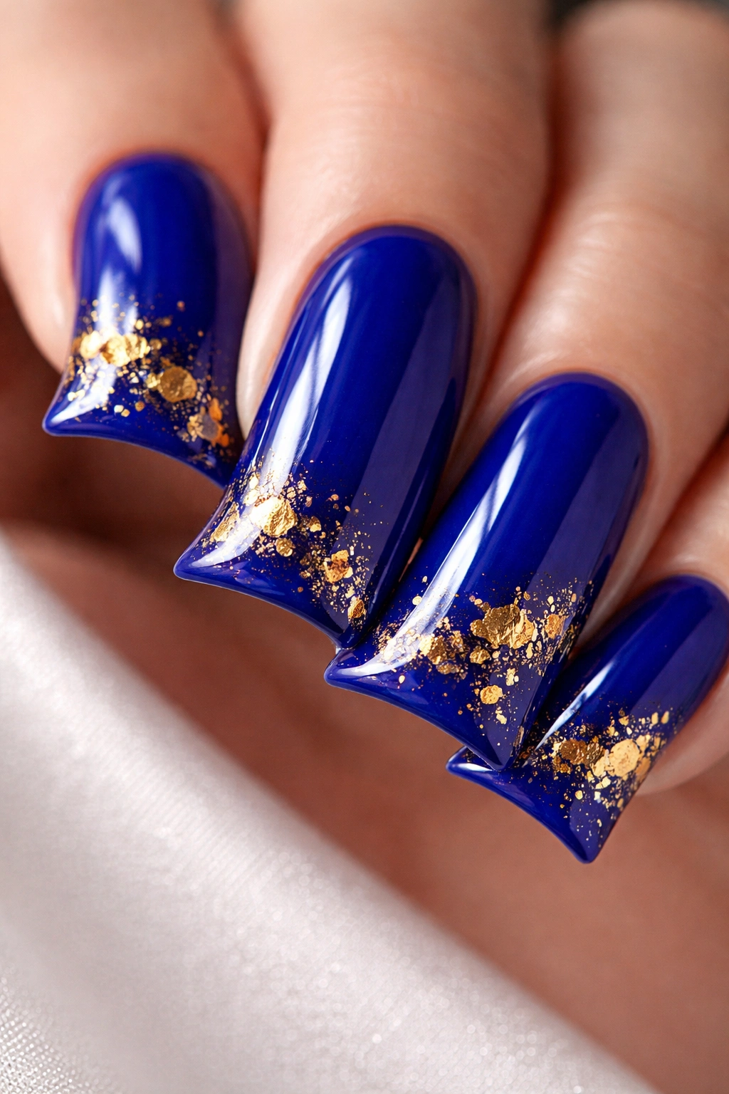 Close-up of a duck nail with glossy royal blue finish and gold foil accents