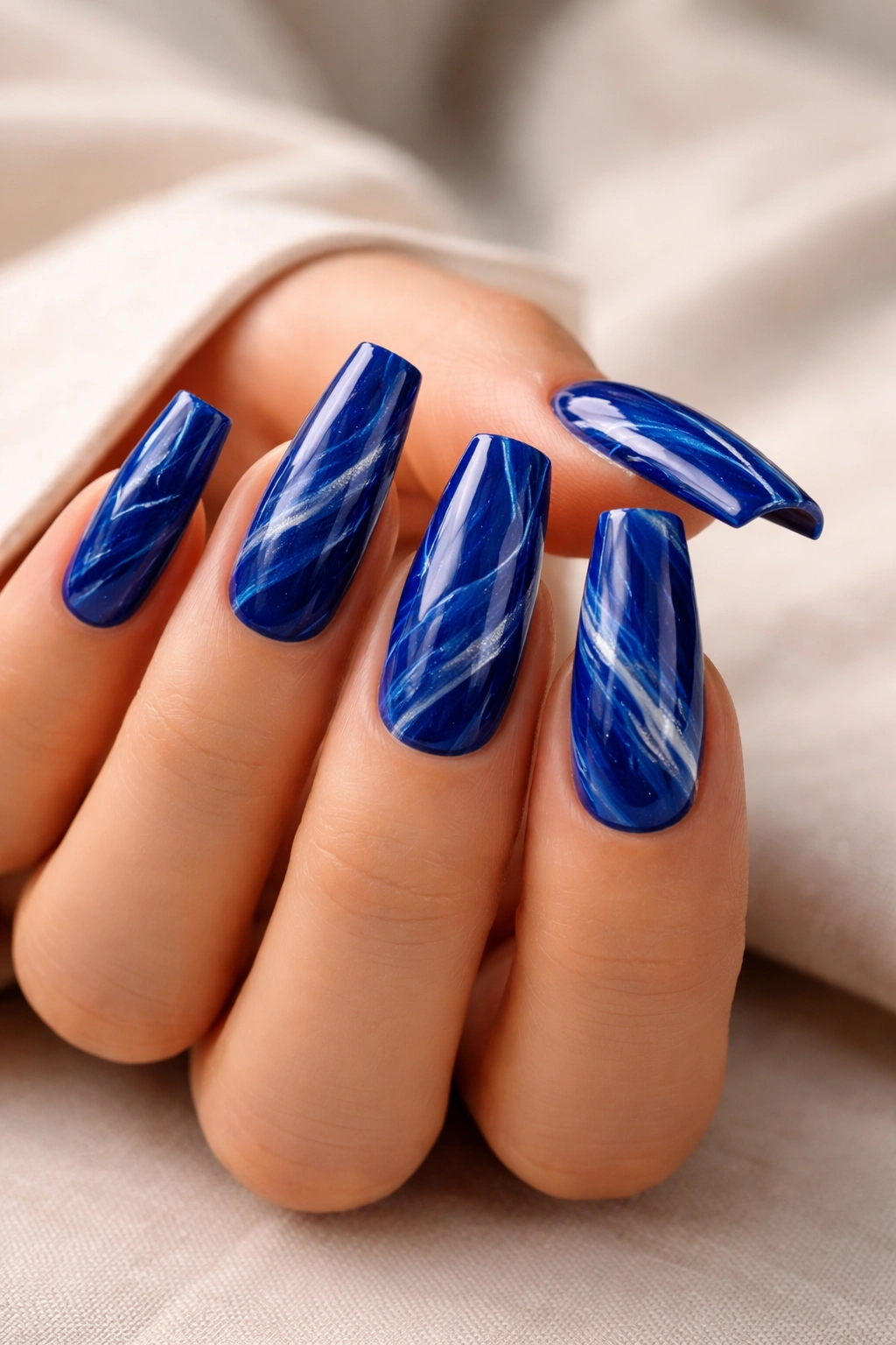 Close-up of royal blue coffin nails with marble swirls on a neutral backdrop