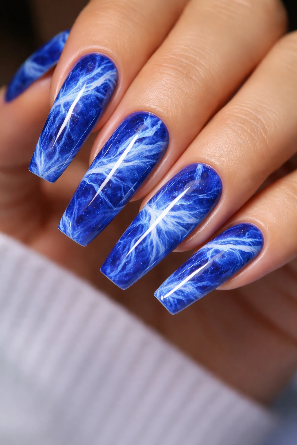 Close-up of royal blue marble nails with white veining