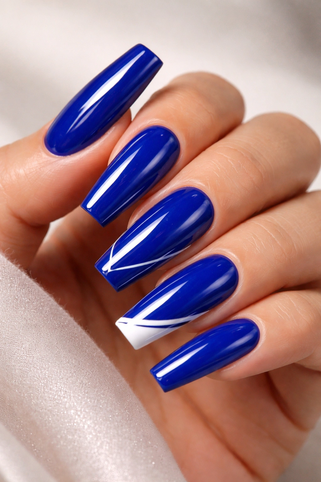 Glossy royal blue nails with white accents on a neutral background
