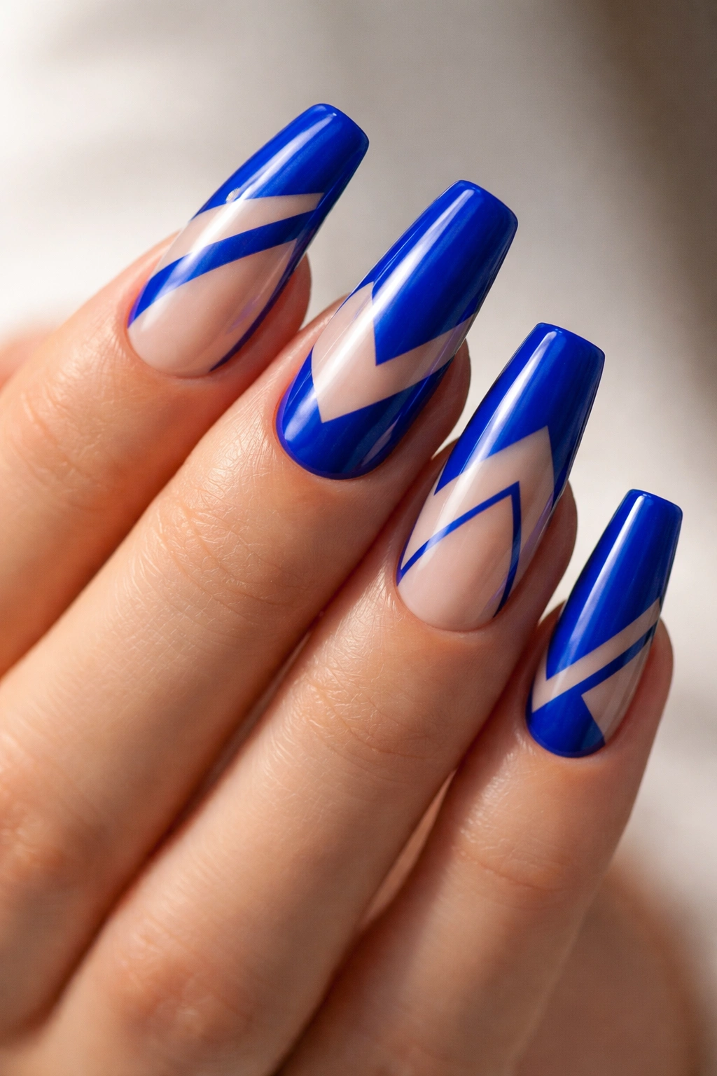 Close-up of medium coffin nails with royal blue polish and negative-space geometric patterns on a bare hand