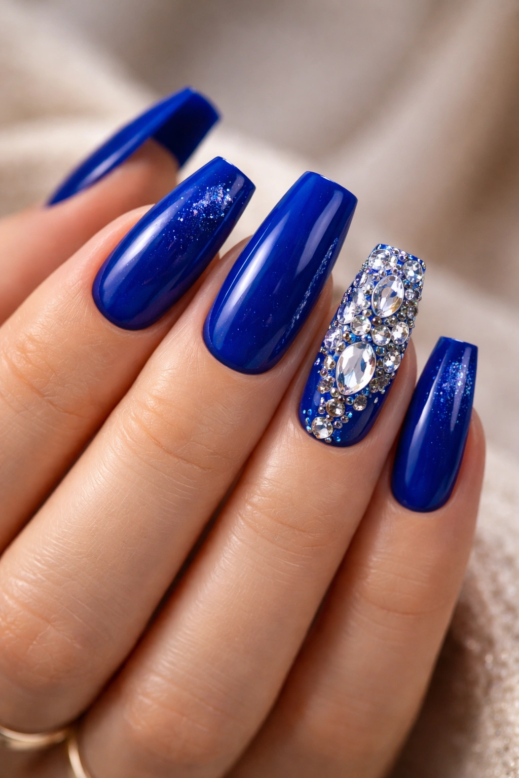 Close-up of royal blue nails with crystal accents on an accent nail, sparkling in studio light