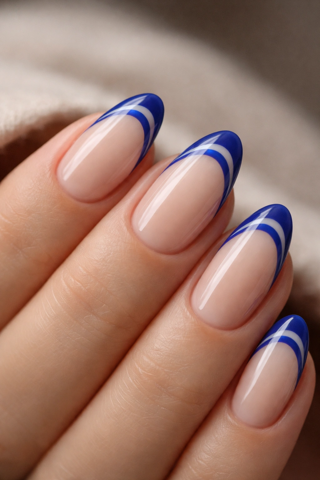 Close-up of a short almond nail with two parallel royal blue tip lines on a nude base.