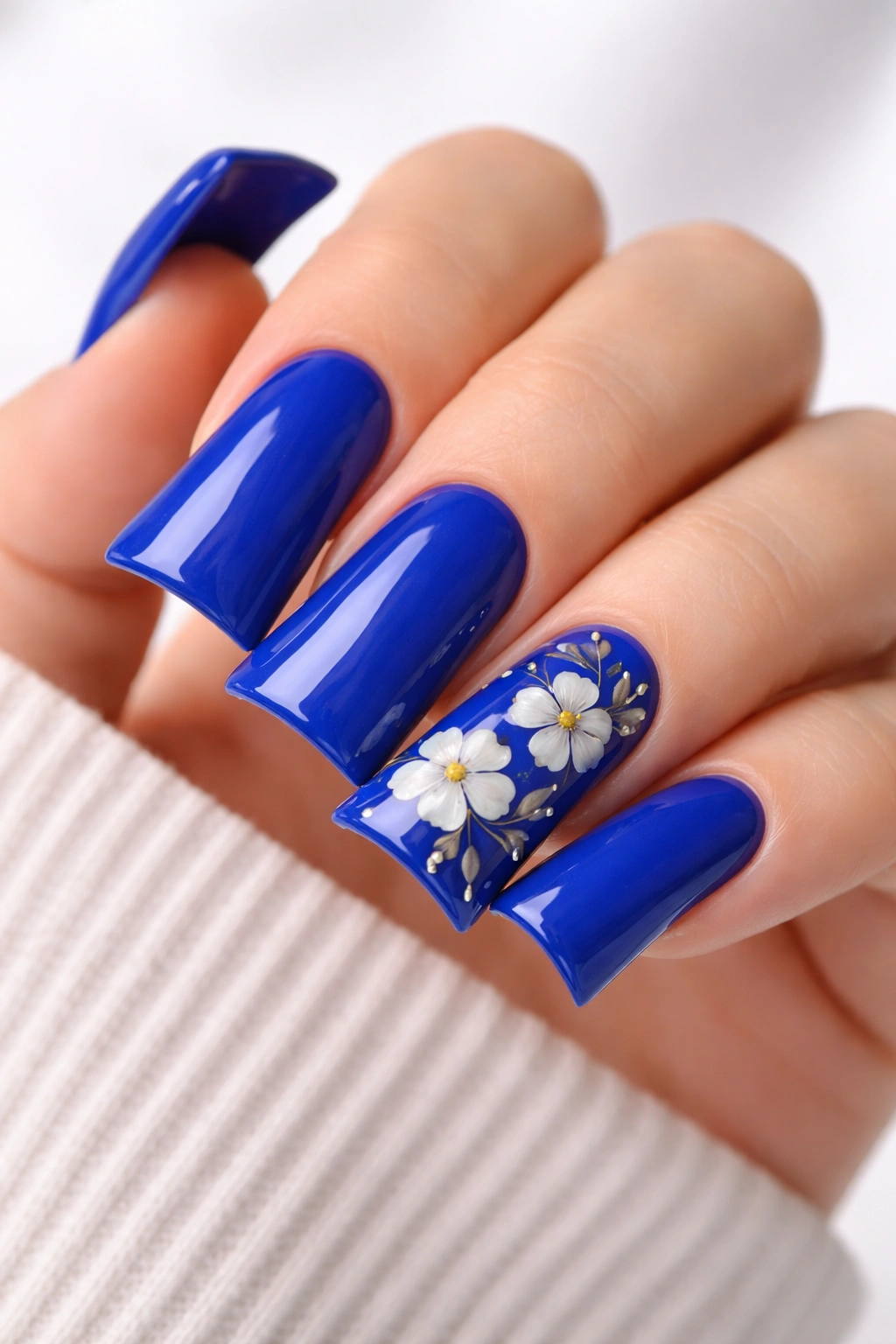 Close-up of duck nails with royal blue polish and a floral accent nail.