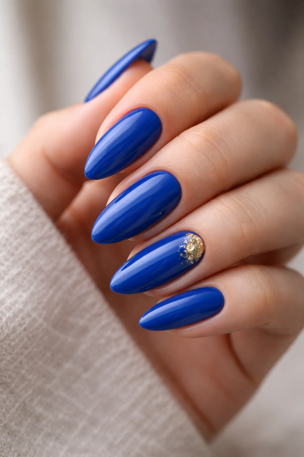 Close-up of royal blue almond nails with subtle gold foil accents on a neutral background.