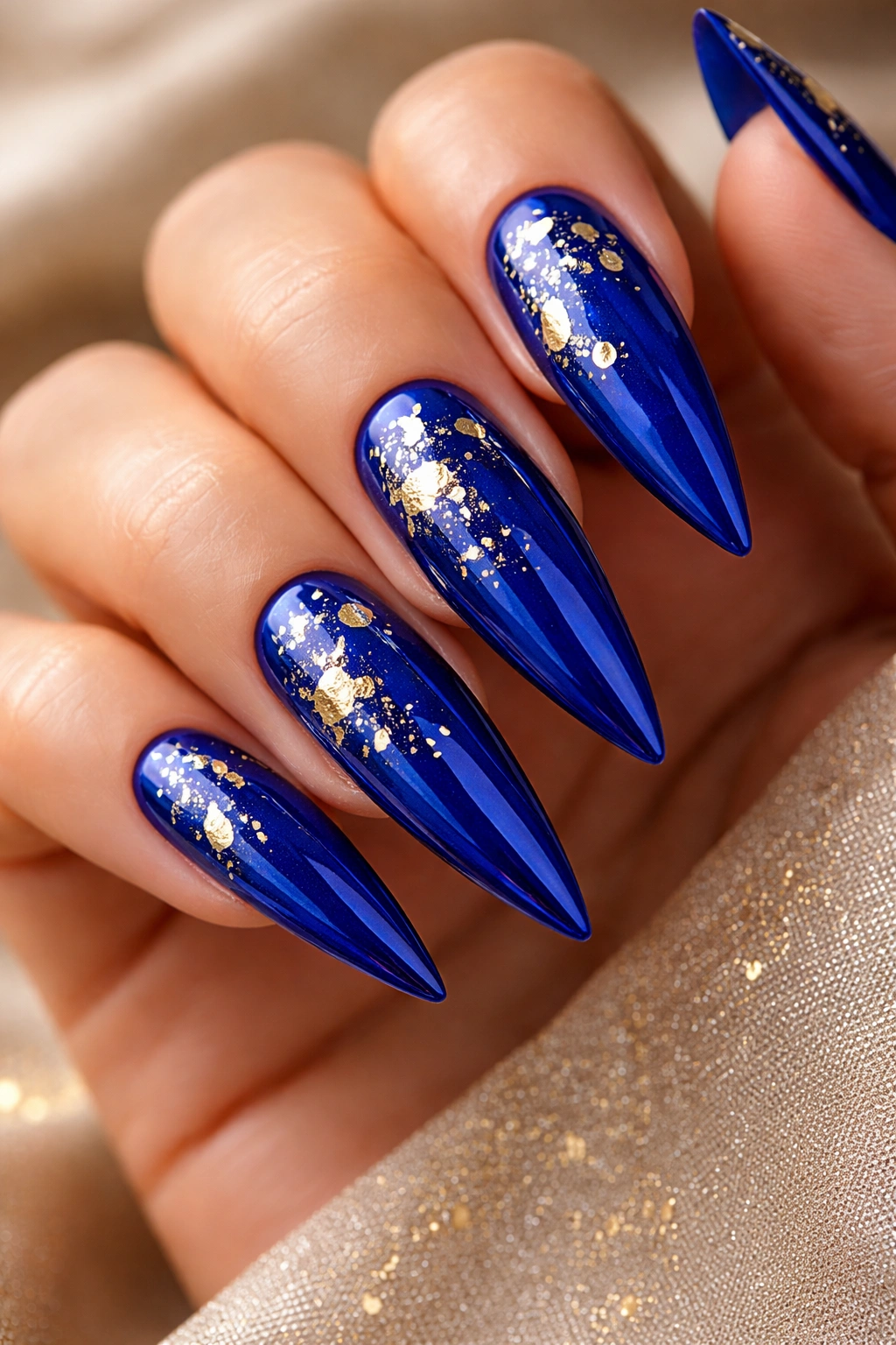 Close-up of glossy royal blue stiletto nails with gold foil accents