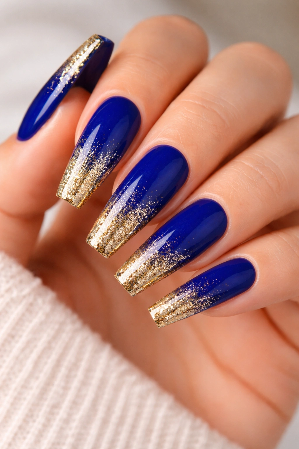 Close-up of coffin nails in royal blue with a gold glitter gradient at tips fading toward base.