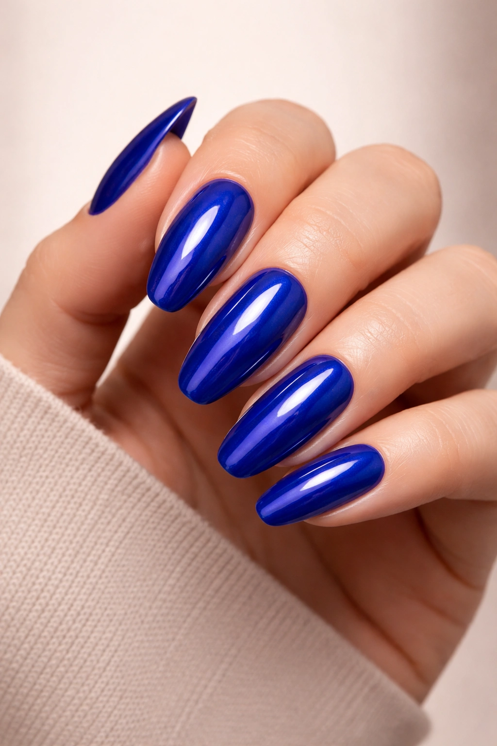 Close-up of royal blue glossy nails on a hand against a neutral background