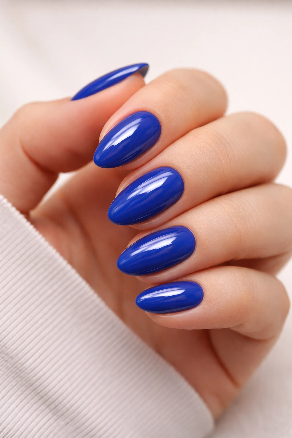 Close-up of short almond nails with solid royal blue gloss on a neutral background