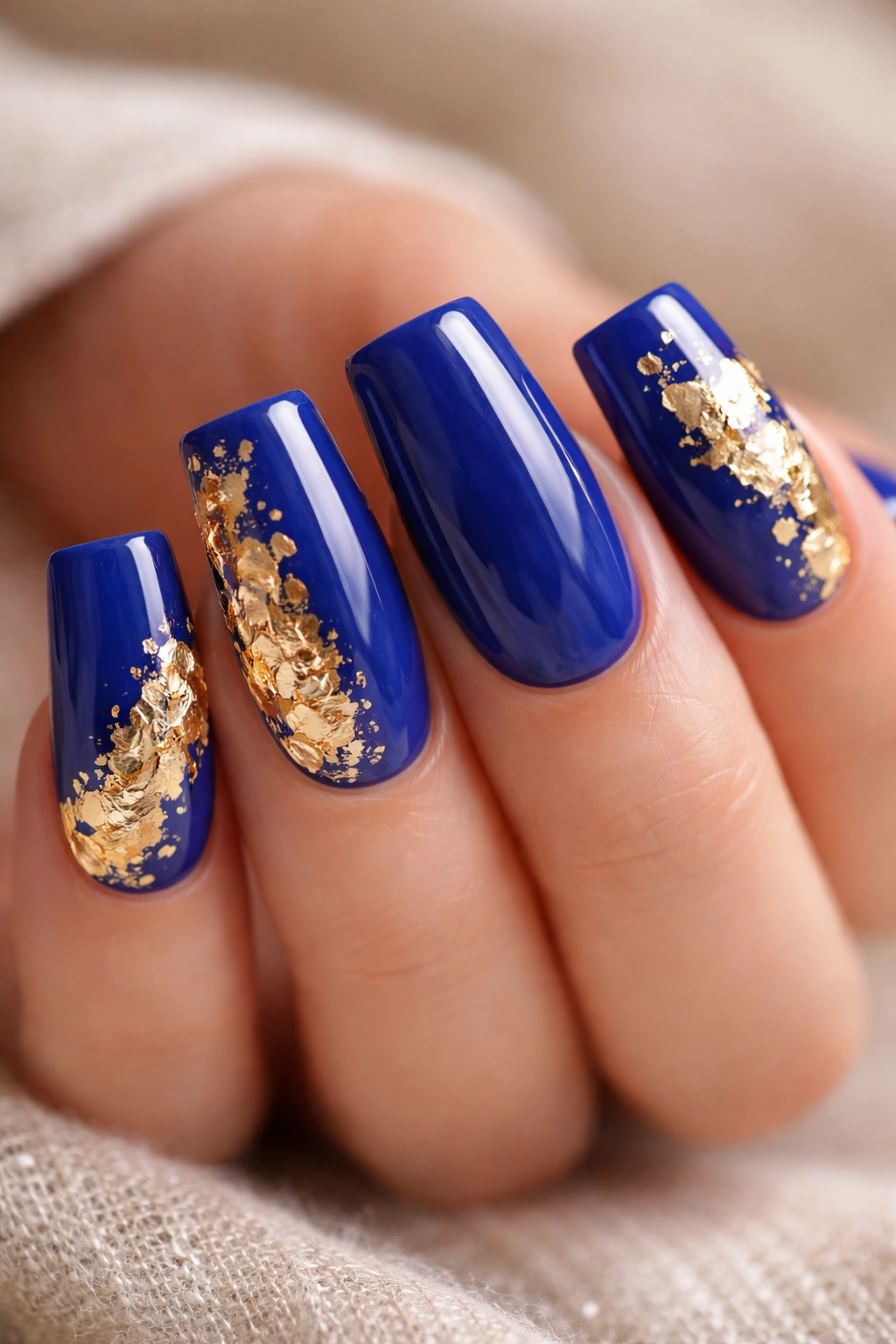 Duck nails with royal blue base and irregular gold leaf accents.
