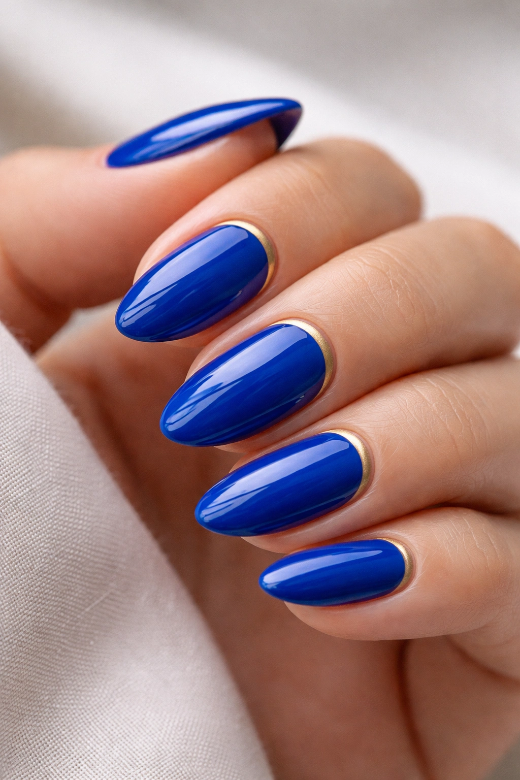 Short almond nails with royal blue gloss and a thin gold stripe