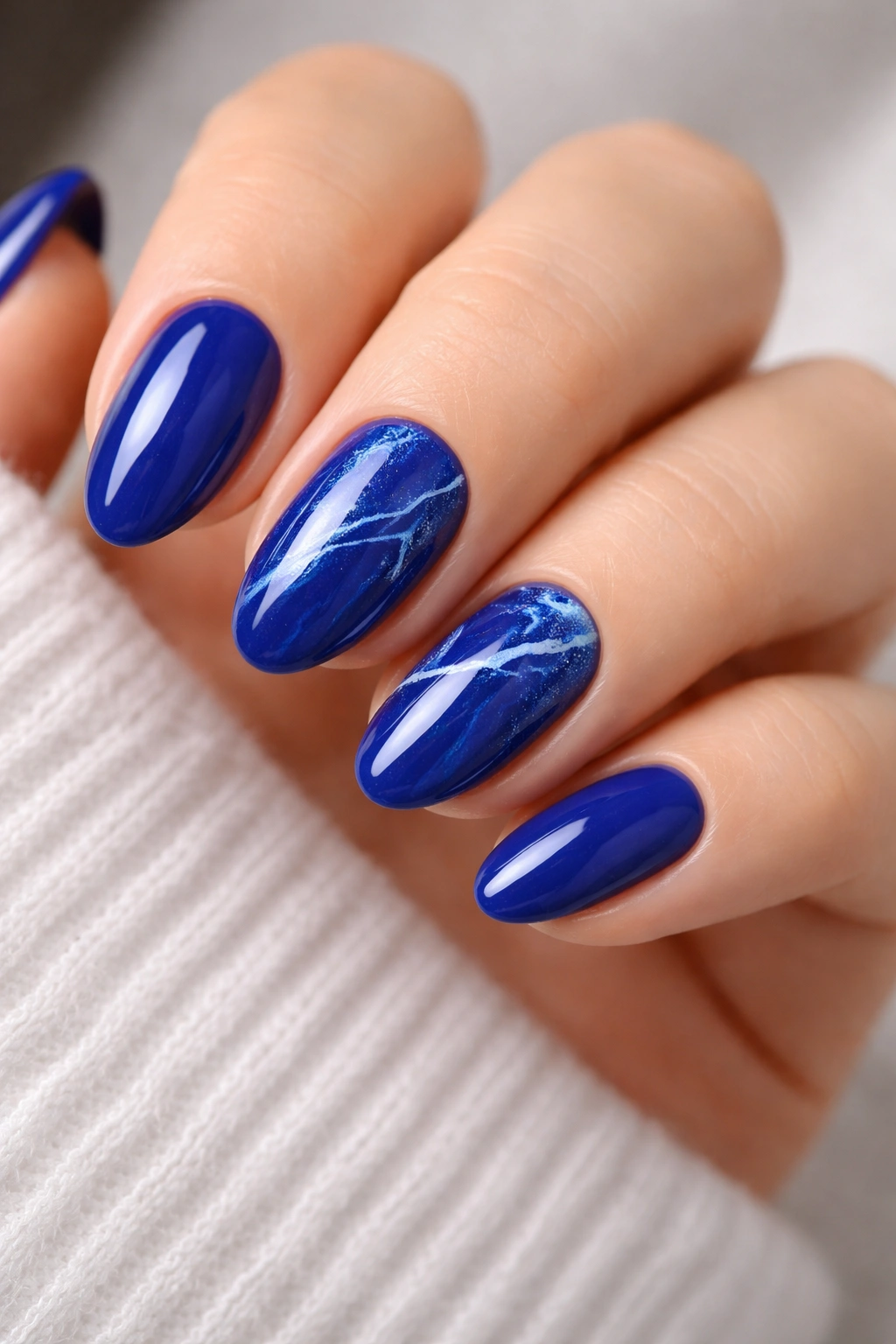 Short almond nails with royal blue marble and white veining on a nude base