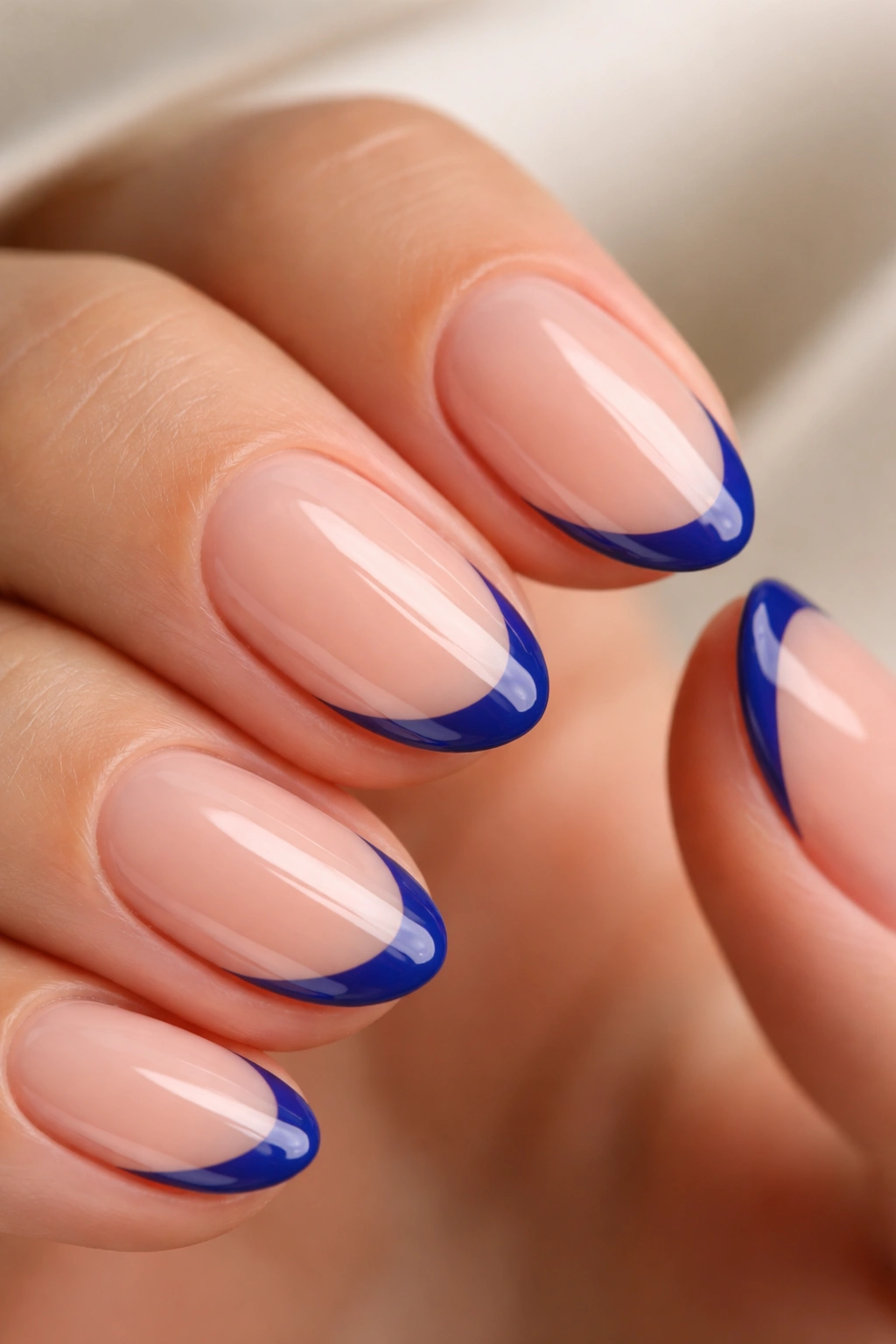 Close-up of a short almond nail with a thin royal blue micro French tip on a nude base