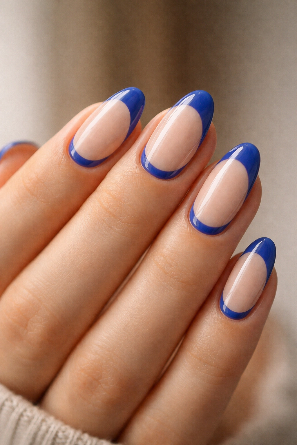 Close-up of short almond nails featuring royal blue half-moon near the cuticle on a nude base