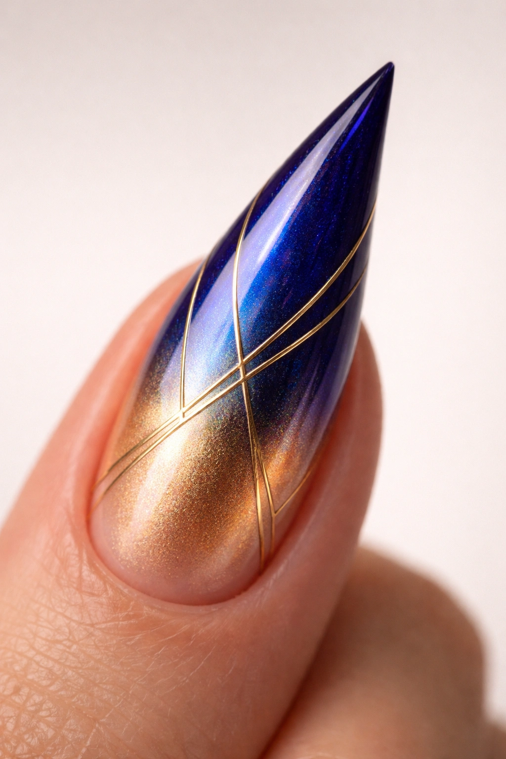 Close-up of a stiletto nail with royal blue to gold ombre and gold geometric lines.