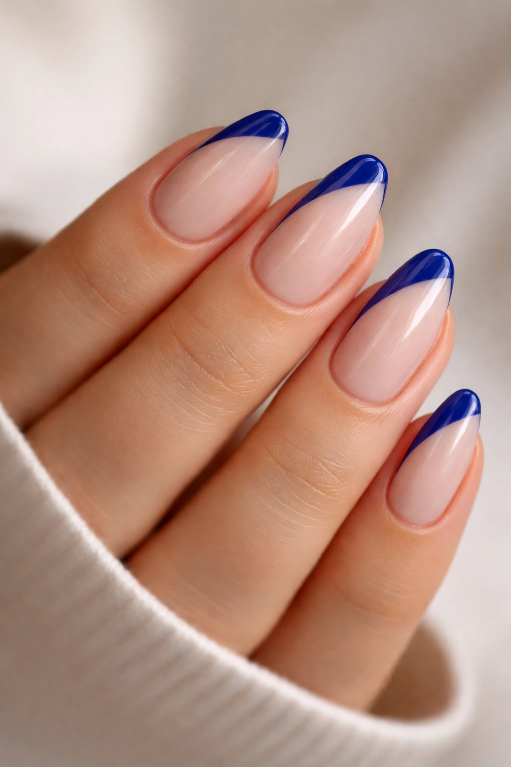 Close-up of short almond nails with a diagonal royal blue edge on a neutral background.