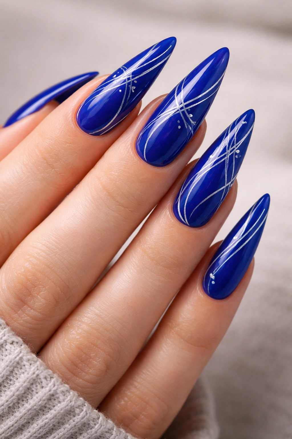 Royal blue nails with silver lines and shapes on stiletto tips