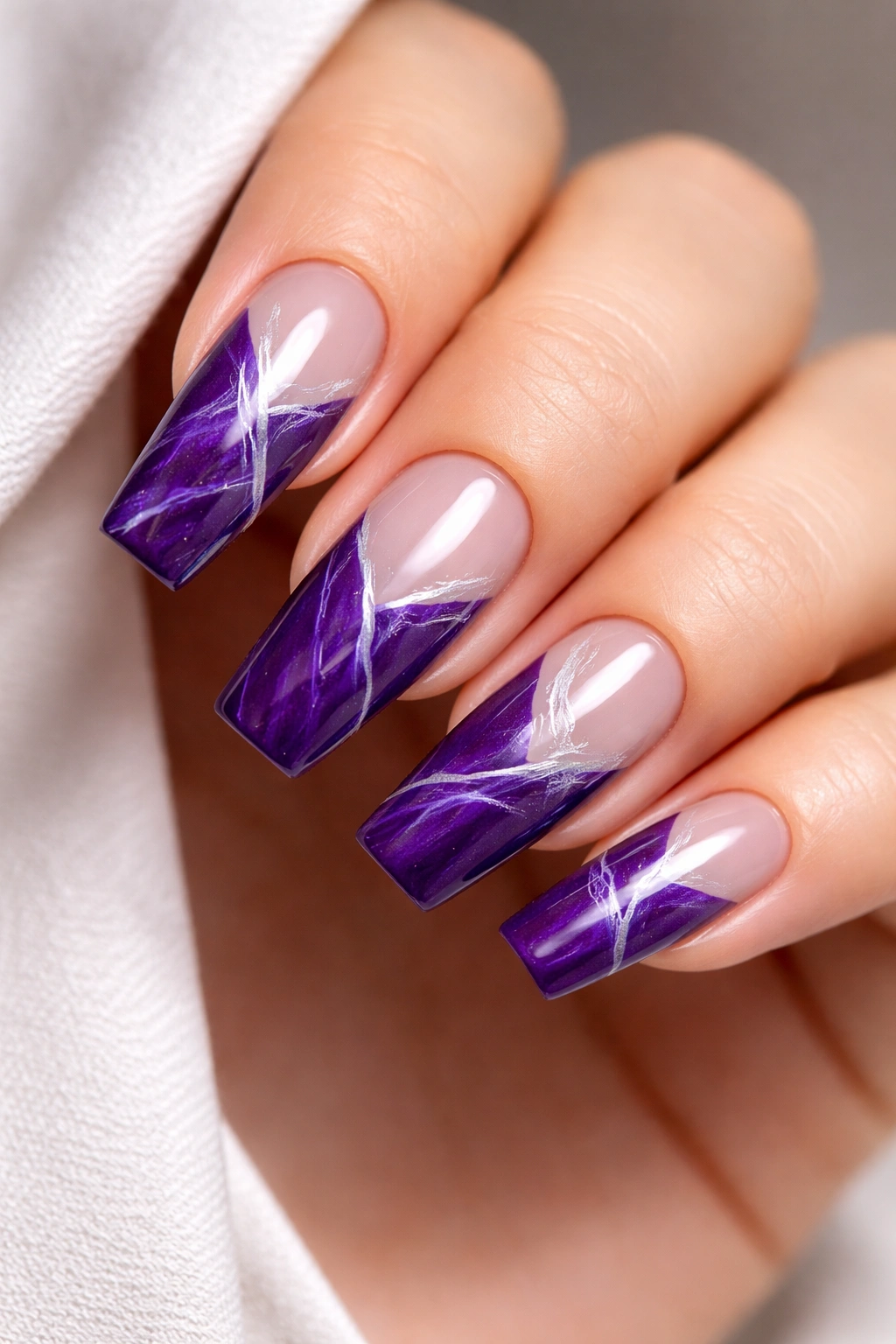 Close-up of coffin nails featuring royal purple with negative space and white marble veining on a natural nail base