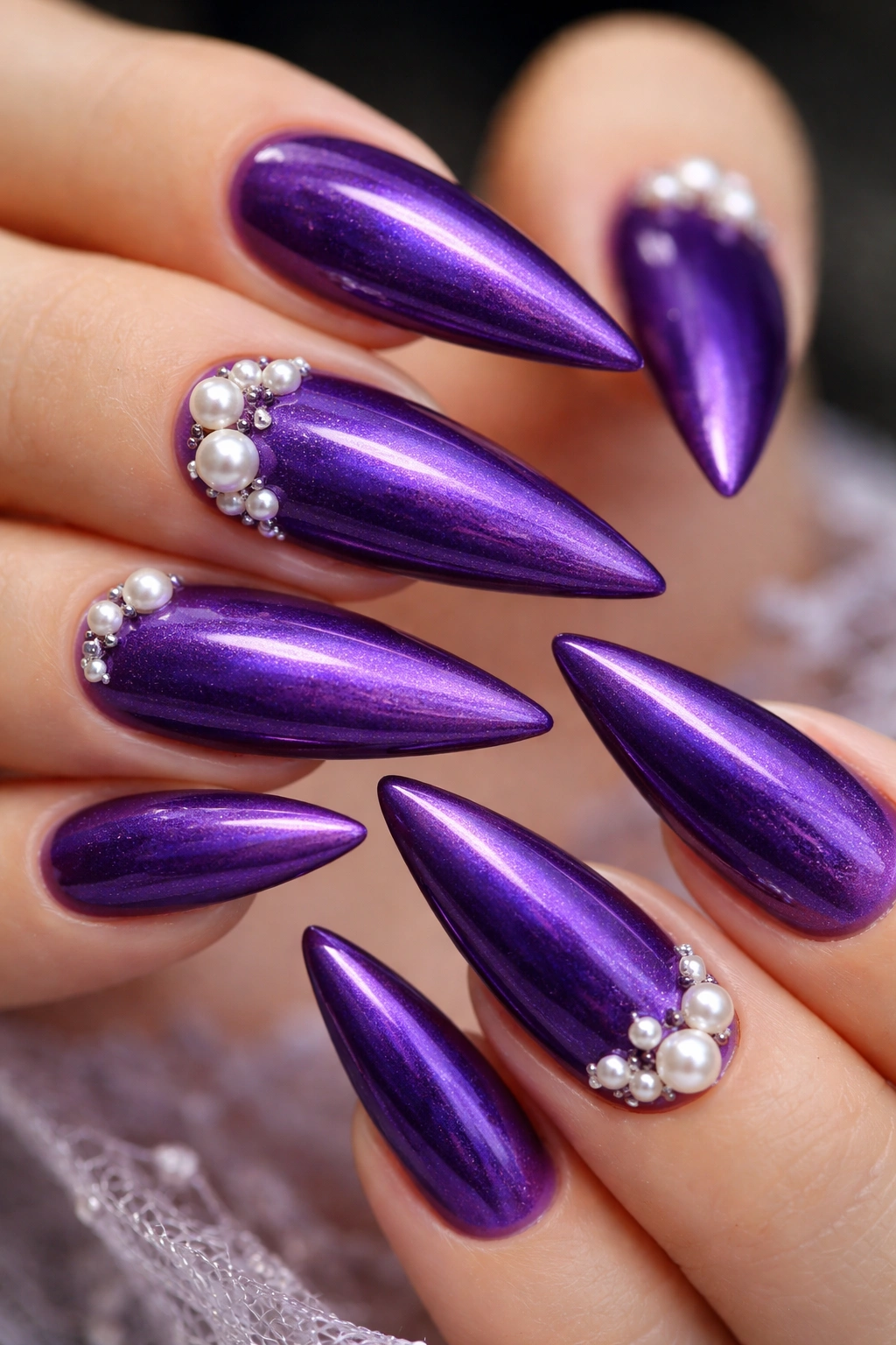 Close-up of royal purple nails with pearl accents on stiletto tips