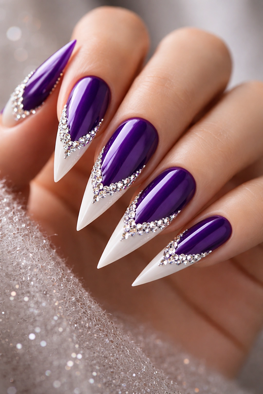 Close-up of royal purple stiletto nails with white tips and rhinestone accents