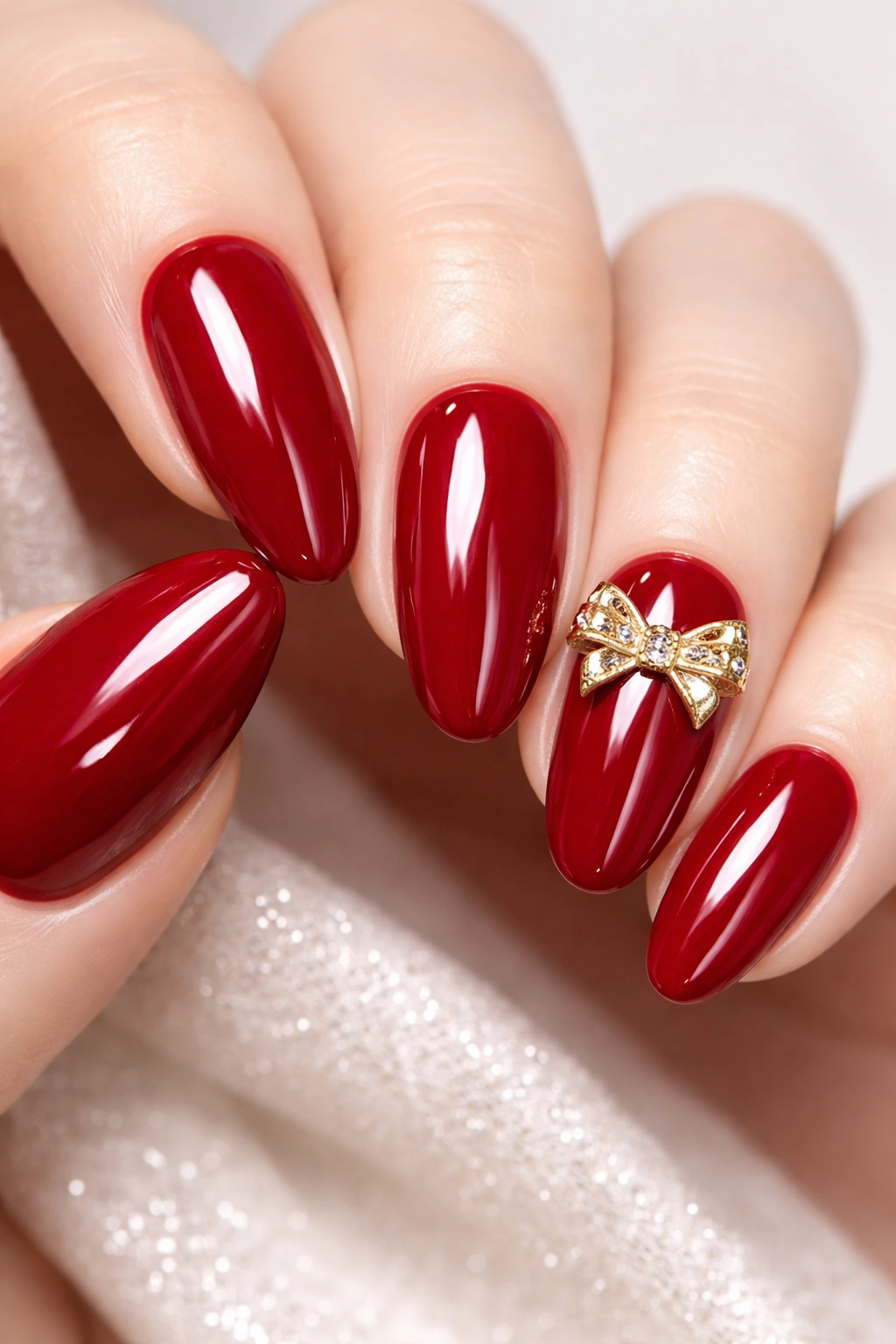 Ruby red nails with small metallic bow accents on a neutral background