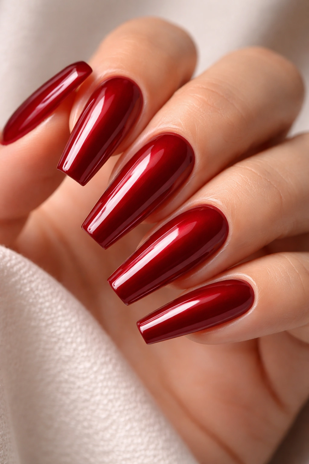 Close-up of deep ruby red nails with a high-gloss gel finish on slender ballerina tips.