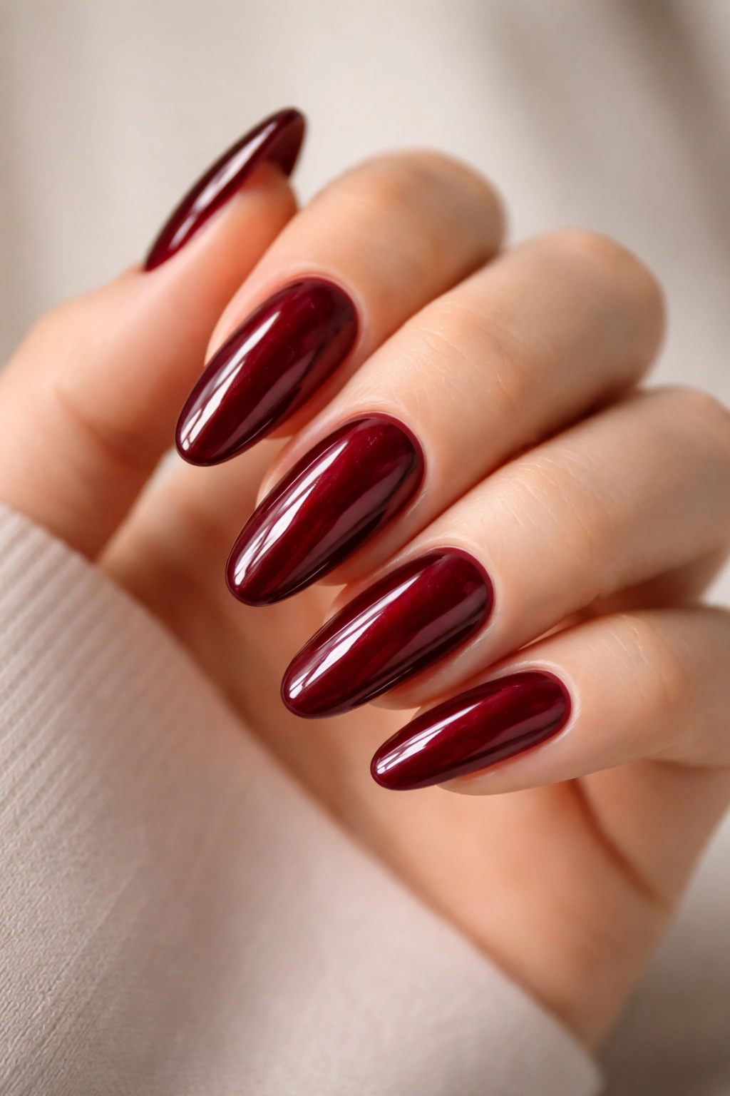 Close-up of long oval nails in deep ruby with glass-like shine.