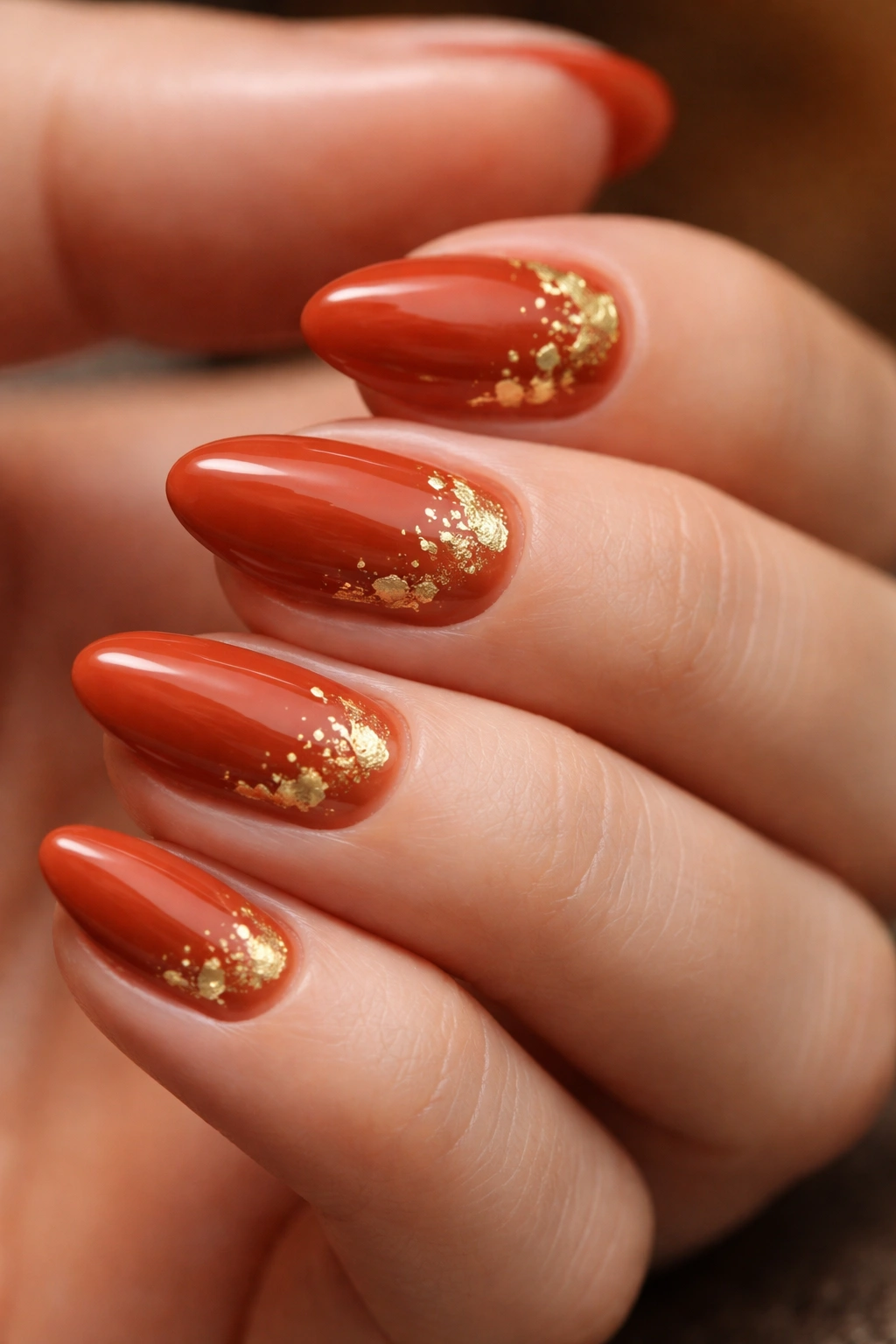 Close-up of rust orange nails with gold foil accents on short almond shape