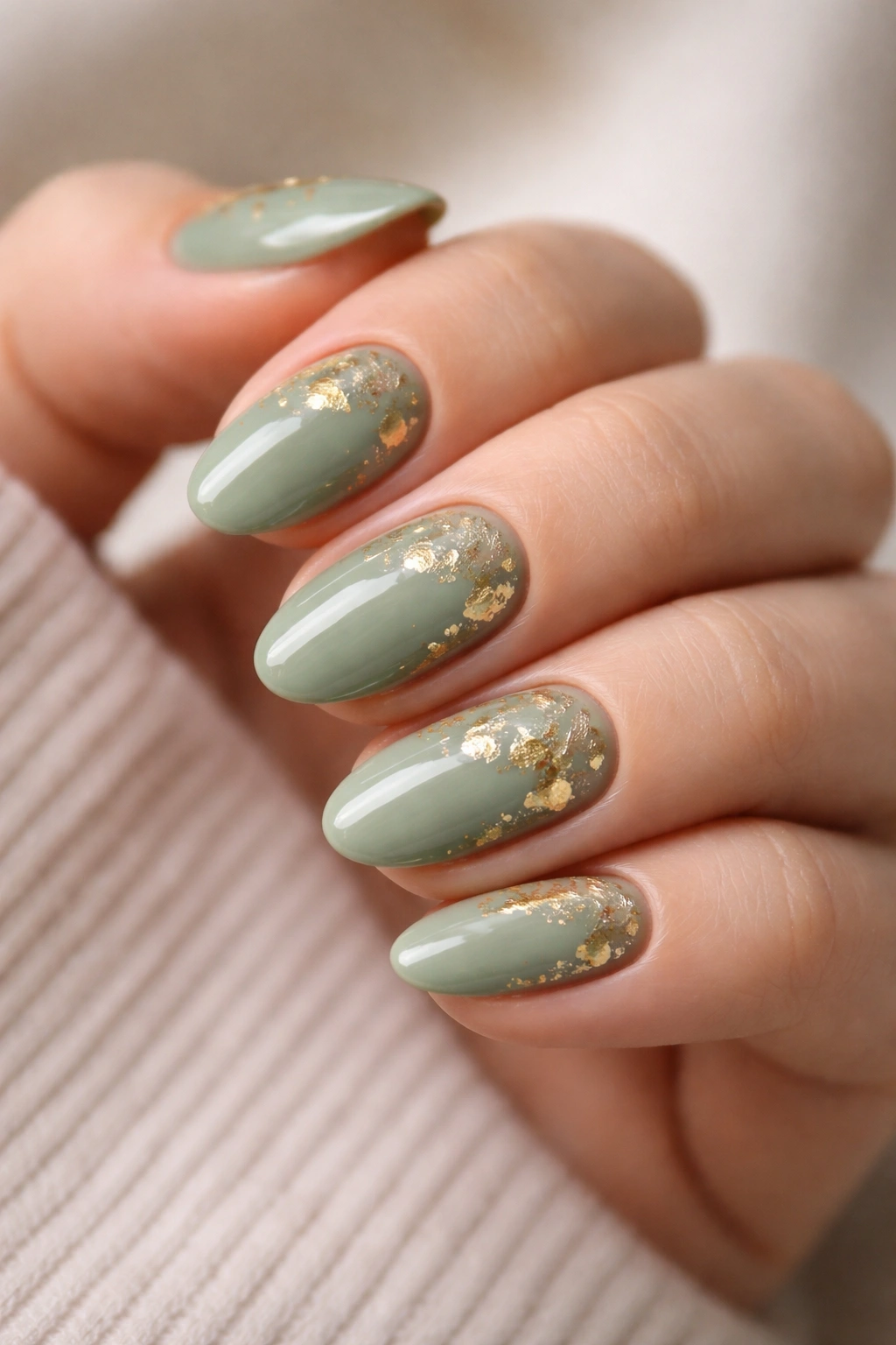 Close-up of sage green nails with gold foil accents on short almond nails