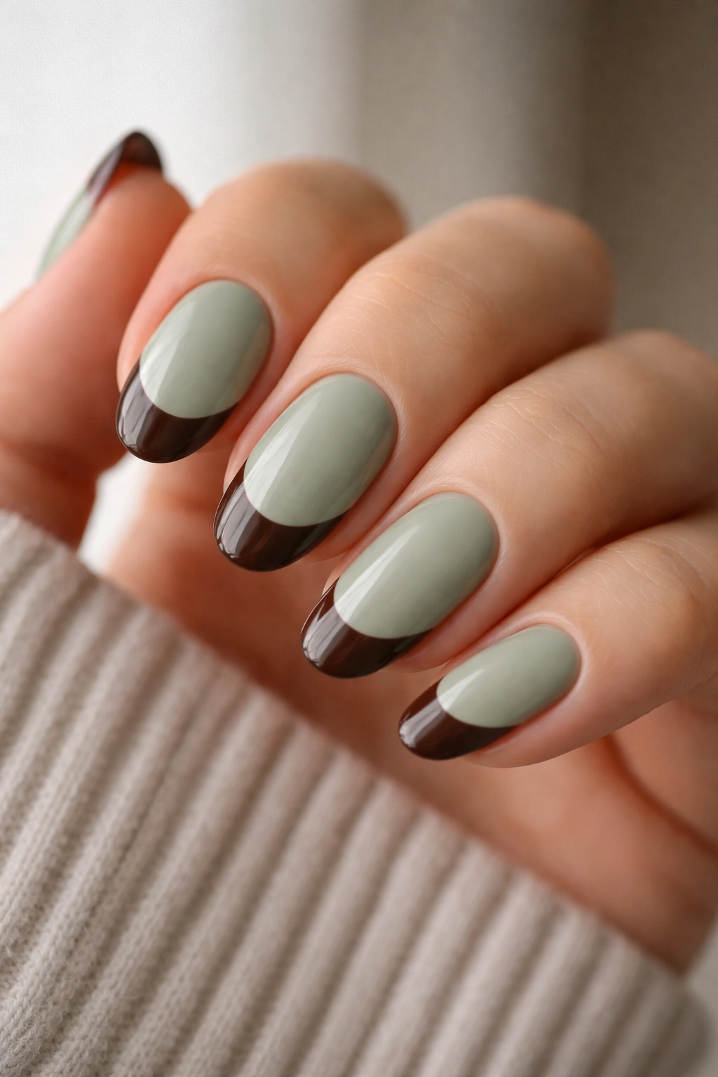 Close-up of short almond nails with sage green base and brown tips.