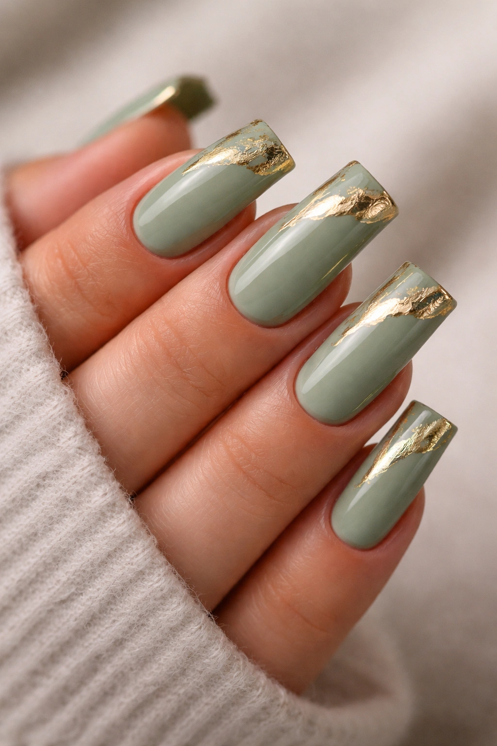 Close-up of sage green nails with irregular gold brushstrokes on medium duck nails