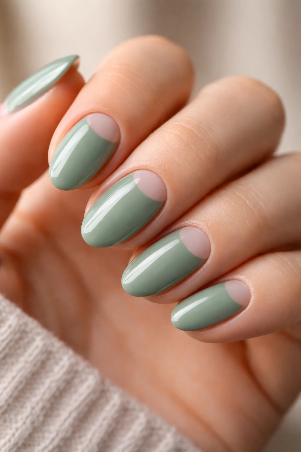 Close-up of short almond sage green nails featuring a negative-space design
