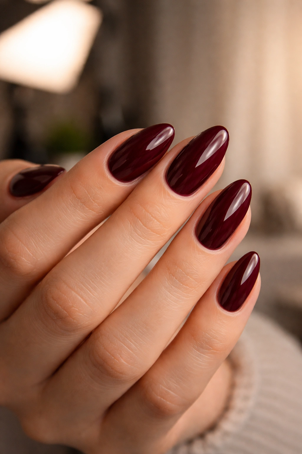 Close-up of a hand with short almond nails in wine-red glossy polish, photographed in a salon photo shoot setting
