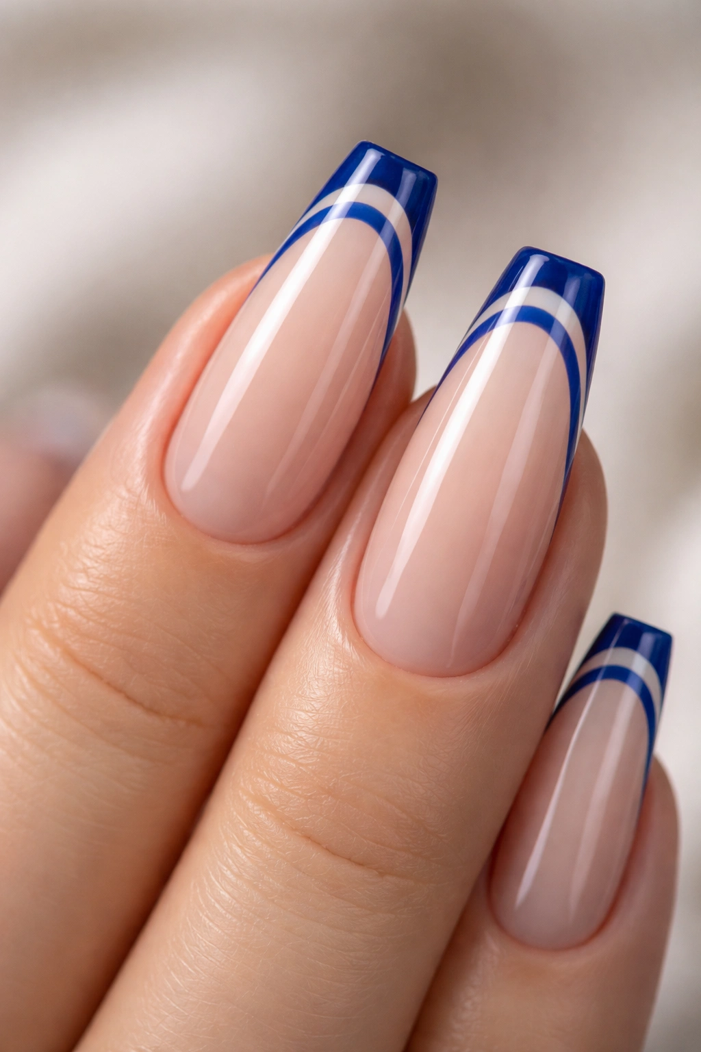 Close-up of a nude ballerina nail with twin sapphire French lines and negative space