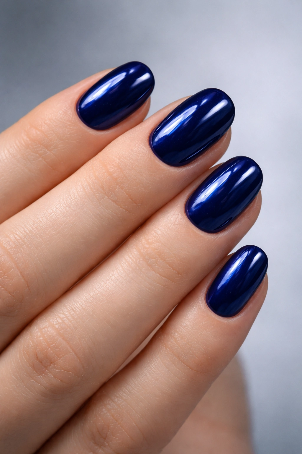 Close-up of short oval nails painted deep sapphire with a glassy finish