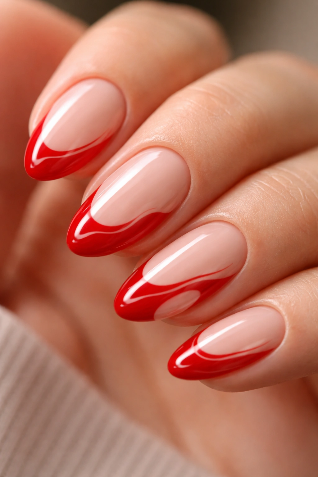 Close-up of a short almond nail with scarlet red swirl along the tip against a neutral background
