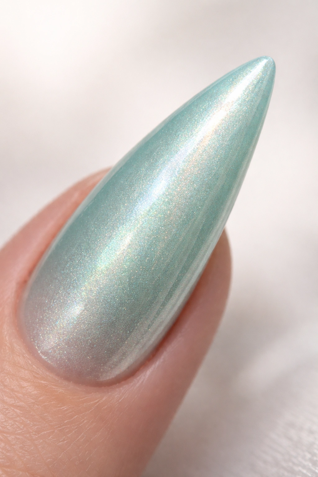 Close-up of a single seafoam green stiletto nail with pearl finish.