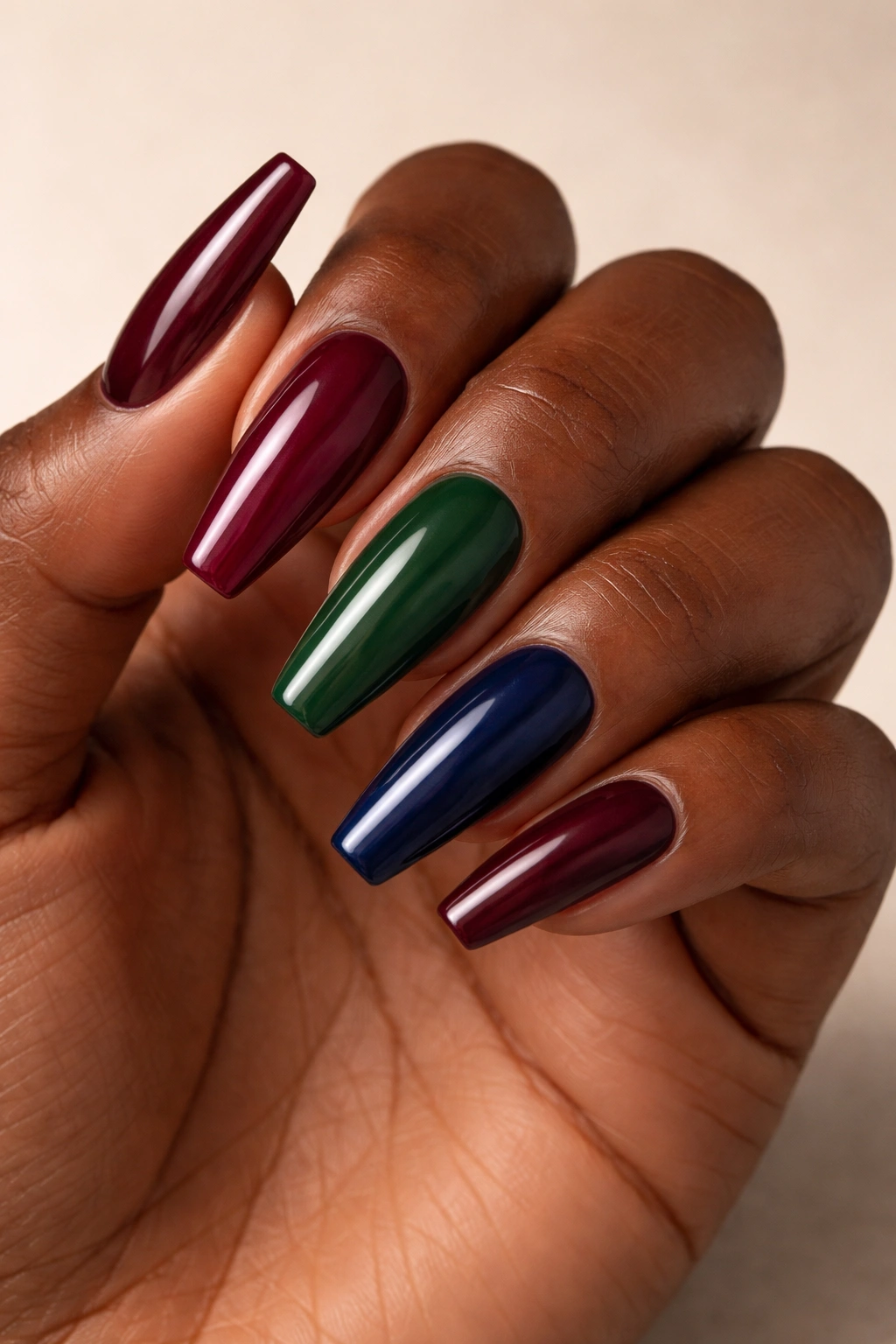 Close-up of a dark-skinned hand with burgundy, forest green, and navy nails.